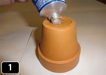 A clay flowerpot upside down with silicon adhesive being squeezed into the hole.
