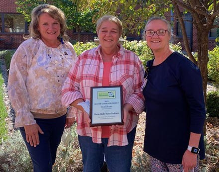 Mela Linn holding her award plaque with Jill Williams to her right and Jane Young to her left.