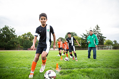 Youth practicing soccer while a coach watches