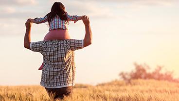 A man carrying a young girl on his shoulders in a field.