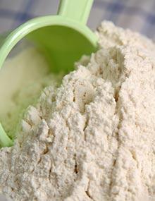 A green measuring cup dipping into white flour.