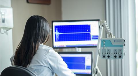 Individual in lab coat seated in front a equipment and monitors