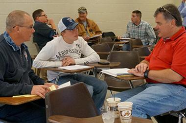 A group sitting on desks in a class having a discussion.