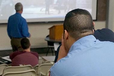 A man sitting in a classroom watching a presentation.