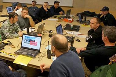 A group sitting around a table with computers and walkie talkies.