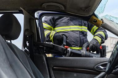 A firefighter cutting a door off a car.