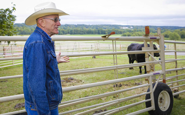 Eldon Cole standing in front of a field with a cow